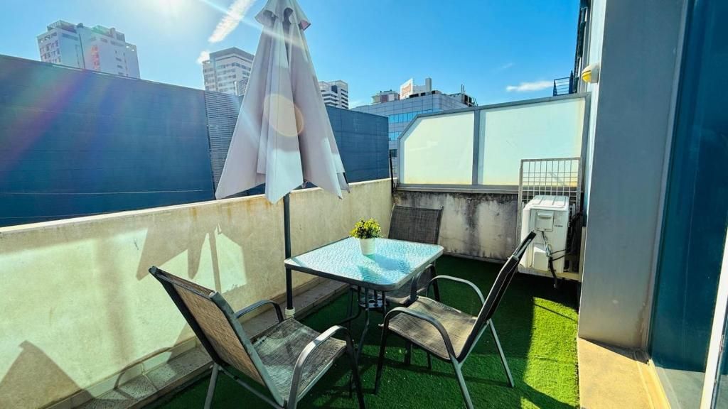 Une terrasse sur le toit avec une table et des chaises, une petite table avec une tasse, et un parasol blanc.