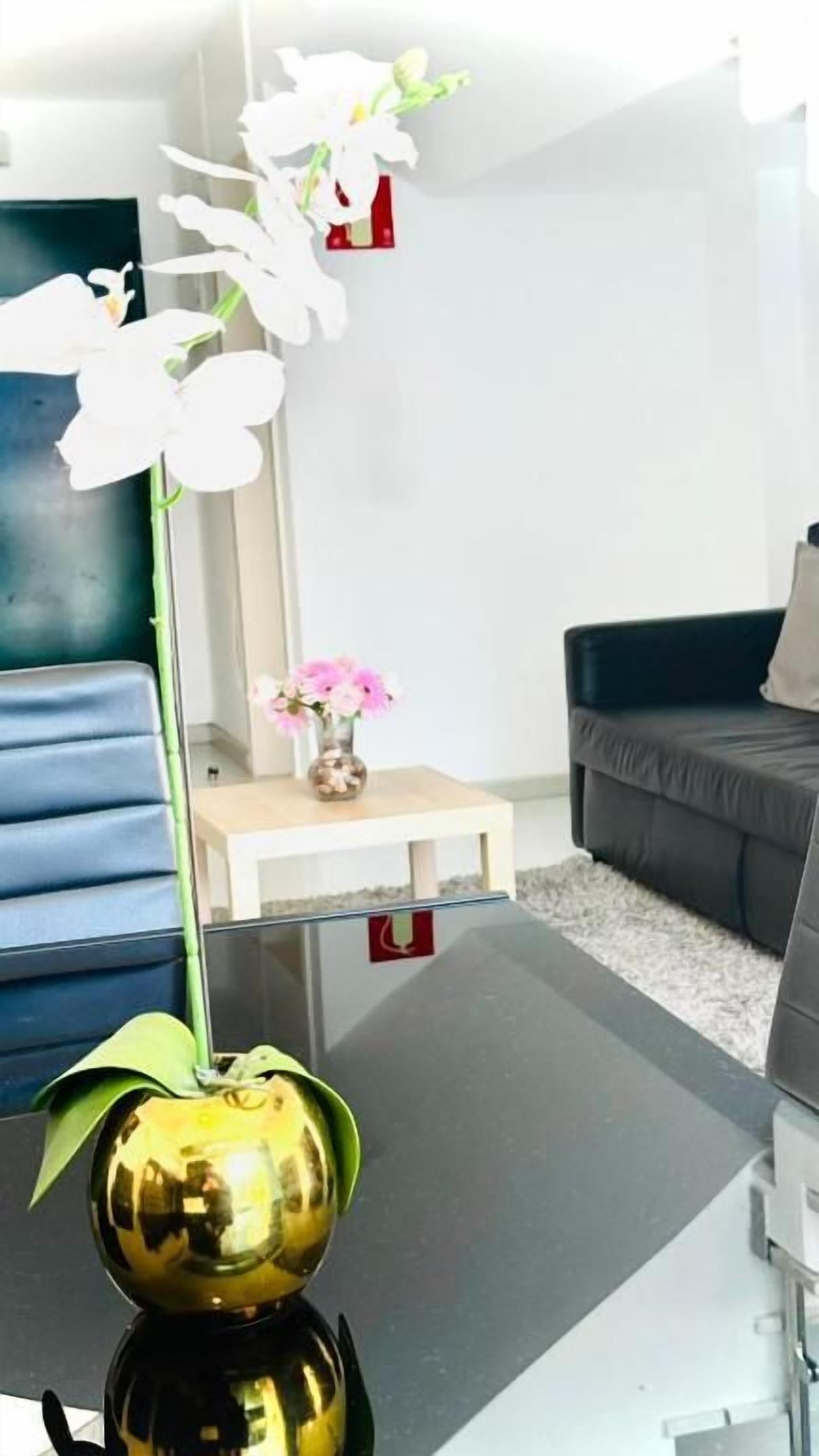 Un salon moderne avec une table basse en verre, un canapé bleu, un canapé foncé et une petite table d’appoint blanche sur laquelle est posé un vase de fleurs.