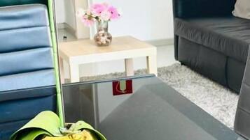 Un salon moderne avec une table basse en verre, un canapé bleu, un canapé foncé et une petite table d’appoint blanche sur laquelle est posé un vase de fleurs.