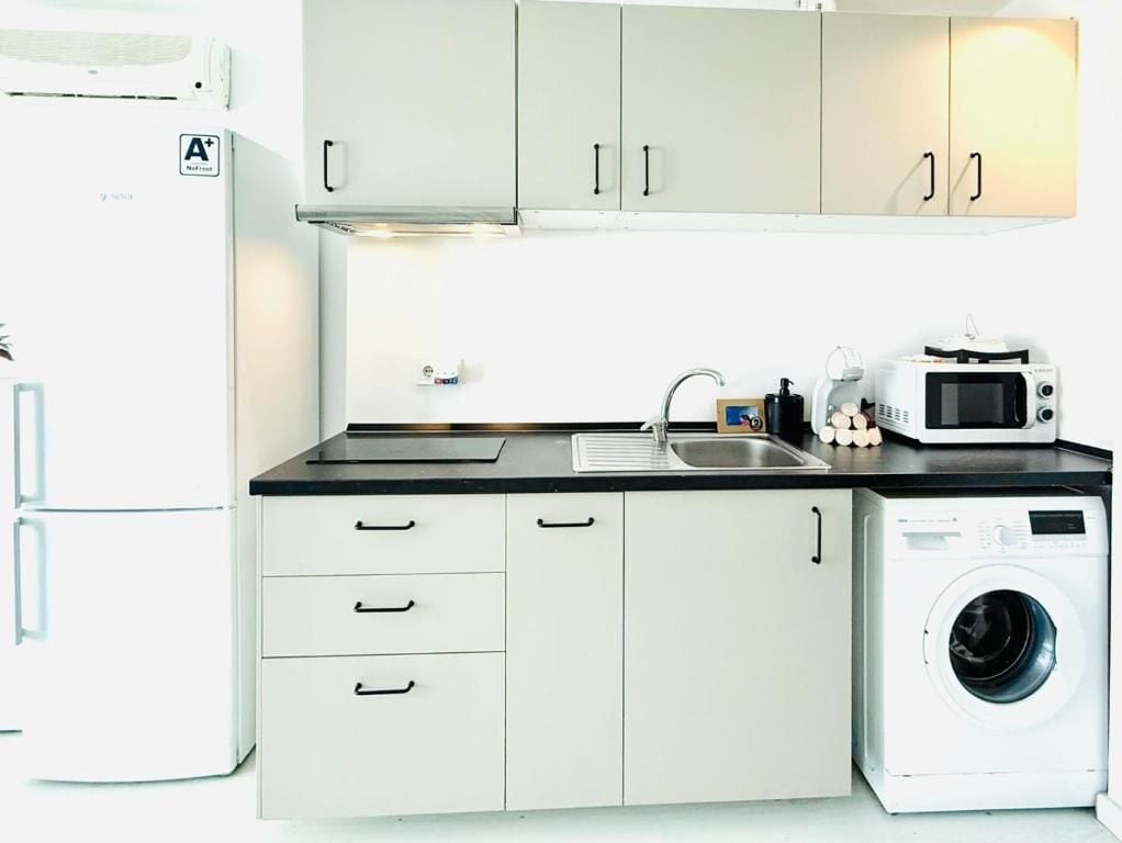 A compact kitchen with a washing machine, a microwave, and a refrigerator.