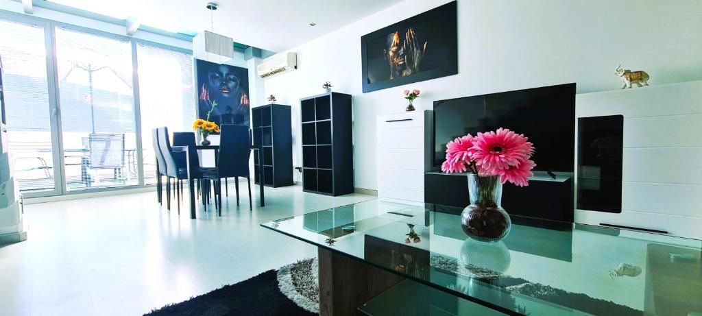 Un salon moderne avec une table basse en verre, un coin repas avec des chaises et un téléviseur fixé au mur.