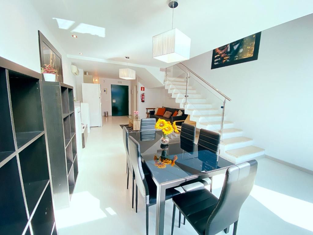 Un espace repas moderne avec une table en verre, des chaises noires et un escalier menant à une autre pièce.