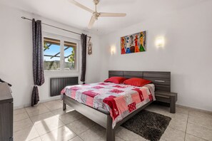 A bedroom with a bed, a nightstand, a wall-mounted artwork, a ceiling fan, and a window with curtains. - La Treille de Saint-Marc by sur la mer (Camps-la-Source)