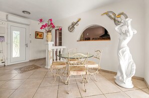 A dining area with a round glass table and four chairs, a white statue, and a wall-mounted guitar. - La Treille de Saint-Marc by sur la mer (Camps-la-Source)
