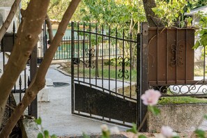 A gated entrance with a metal gate, a concrete pathway, and a tree in the foreground. - La Treille de Saint-Marc by sur la mer (Camps-la-Source)