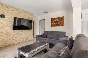 A living room with a stone wall, a flat-screen TV, a grey sofa, a coffee table, and a painting. - La Treille de Saint-Marc by sur la mer (Camps-la-Source)