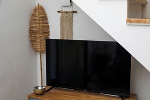A flat-screen TV on a wooden stand, a woven wall hanging, and a bamboo plant. - Kiara Garitsa House - Beautiful 1-bedroom apartment with AC in Corfu Town (Corfu Town)
