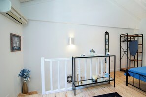 A room with a white crib, a glass table with decorative items, a wooden floor, and a bed with a blue cover. - Kiara Garitsa House - Beautiful 1-bedroom apartment with AC in Corfu Town (Corfu Town)