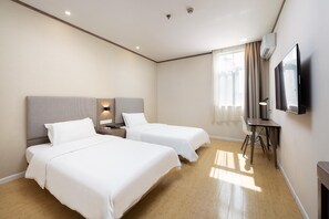 Habitación de hotel con dos camas, un escritorio, una silla, un televisor de pantalla plana y una ventana con cortinas.