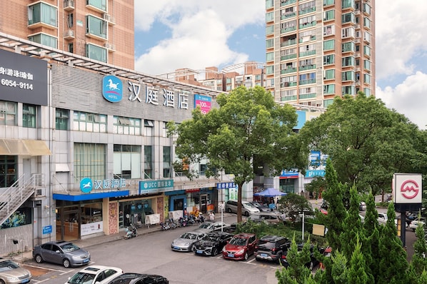 A hotel with a modern facade, multiple floors, and a parking lot in front. - Hanting Hotel Shanghai (Shanghai)