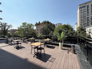 An outdoor seating area with tables and chairs, surrounded by greenery and overlooking a cityscape. - Vinzor (Bishkek)