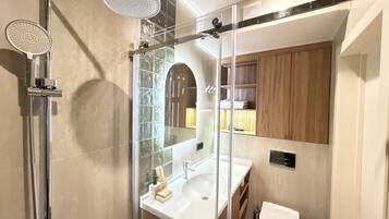 A modern bathroom with a glass-enclosed shower, a white sink, and a wooden vanity.
