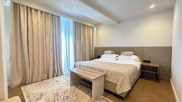 A hotel room with a bed, bedside tables, a nightstand, a small table, and a patterned rug.