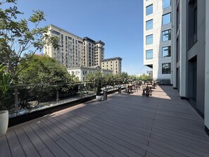 Terraza en la azotea con suelo de madera, mobiliario exterior y vistas de edificios circundantes.