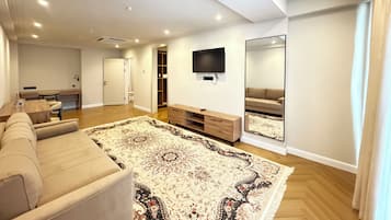 A modern living room with a large sofa, a flat-screen TV, a wooden coffee table, and a patterned rug.