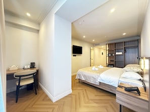 Une chambre d’hôtel équipée d’un lit, d’une table de chevet, d’un bureau, d’une chaise et d’un téléviseur fixé au mur.