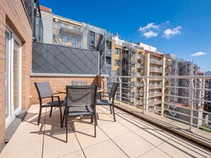 Ein Balkon mit Gartenmöbeln, Blick auf ein Wohngebäude und ein klarer Himmel.