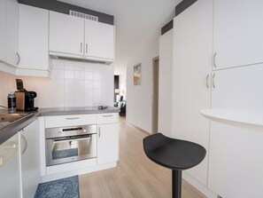 A modern kitchen with white cabinetry, a built-in oven, a coffee machine, and a small black bar stool. - Nice apartment for 2 people with WIFI, TV and terrace (Blankenberge)
