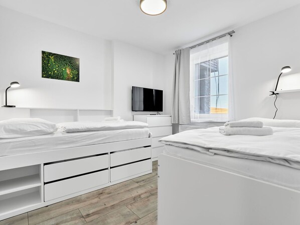 A modern bedroom with two beds, a flat-screen TV, and a large window with curtains.