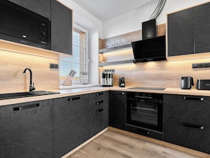 A modern kitchen with dark cabinetry, a stainless steel range hood, a built-in oven, and a window providing natural light.