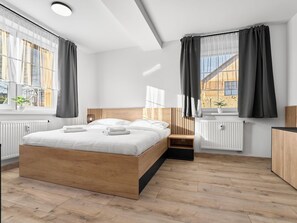 Un dormitorio moderno con una cama de madera, ropa de cama blanca y vistas a un edificio a través de amplios ventanales.
