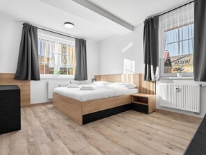 A modern bedroom with a wooden bed, a bedside table, a radiator, and a window with curtains.