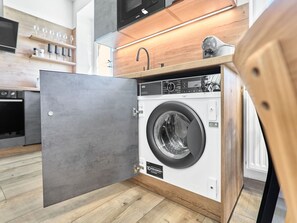 A compact, modern laundry room with a built-in washer and dryer, wooden cabinetry, and a minimalist design.