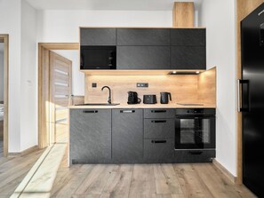 Une cuisine moderne dotée de meubles de rangement aux couleurs sombres, d’un four à micro-ondes, d’une machine à café, d’un grille-pain et d’un four.
