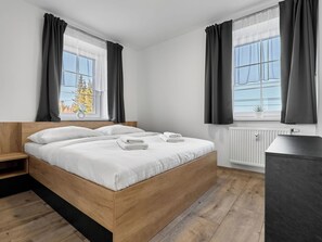 Une chambre à coucher moderne avec un lit en bois, du linge de lit blanc et des rideaux gris.