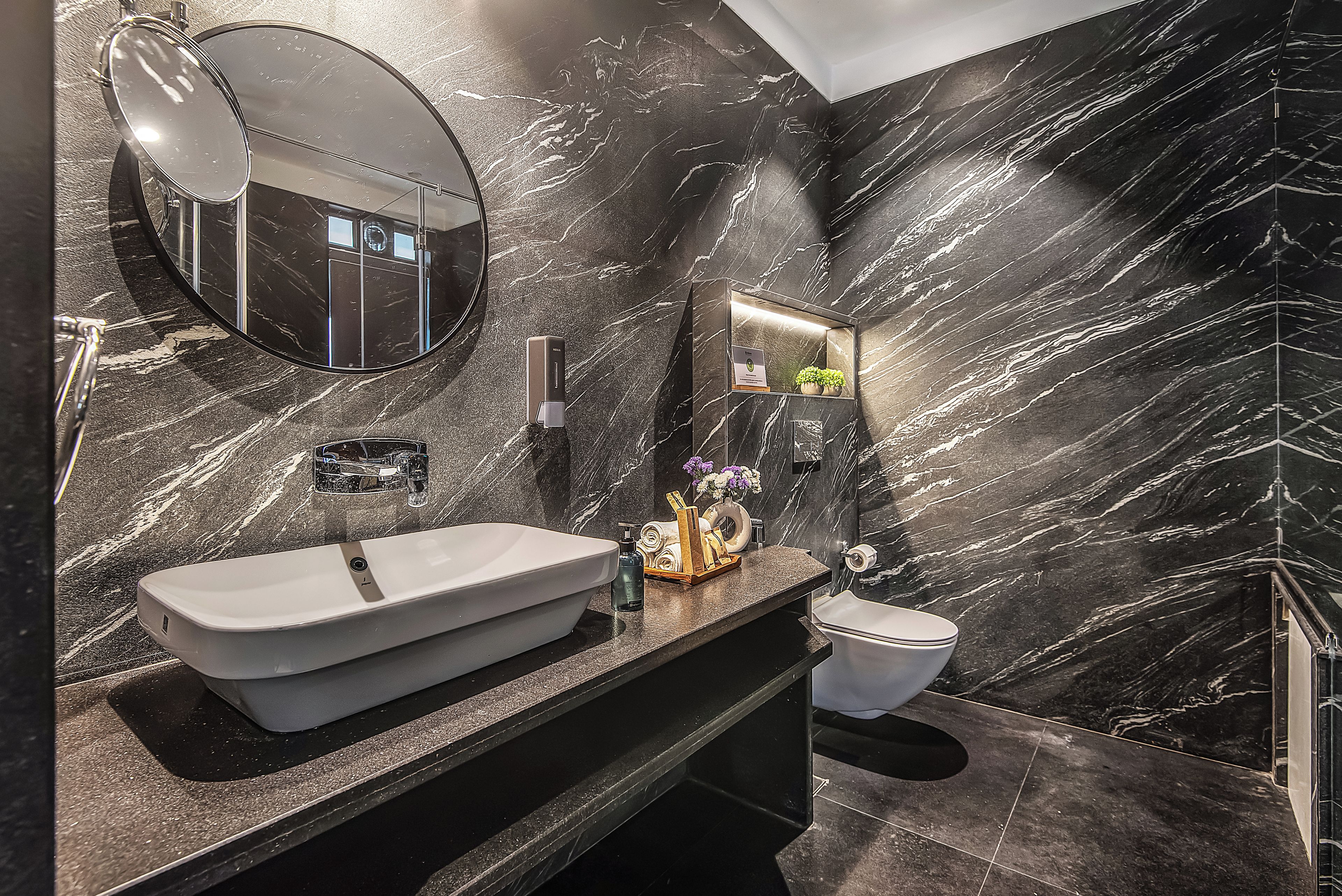 A modern bathroom with a large mirror, a vessel sink, a toilet, and a marble wall.