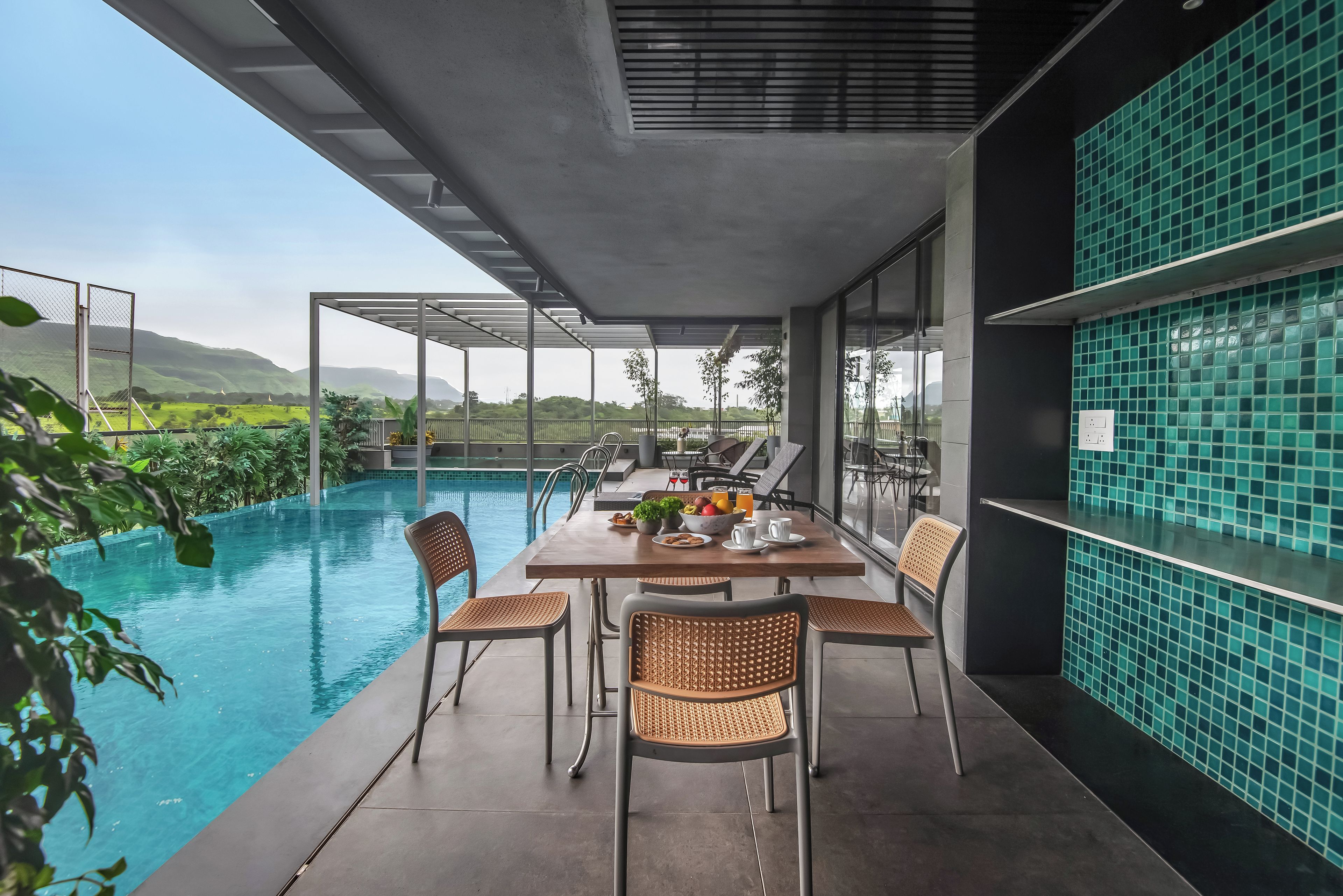 Un área de comedor junto a la piscina con una mesa y sillas, vista a la piscina y una pared de azulejos.