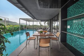 A poolside dining area with a table and chairs, a view of the pool, and a tiled wall.