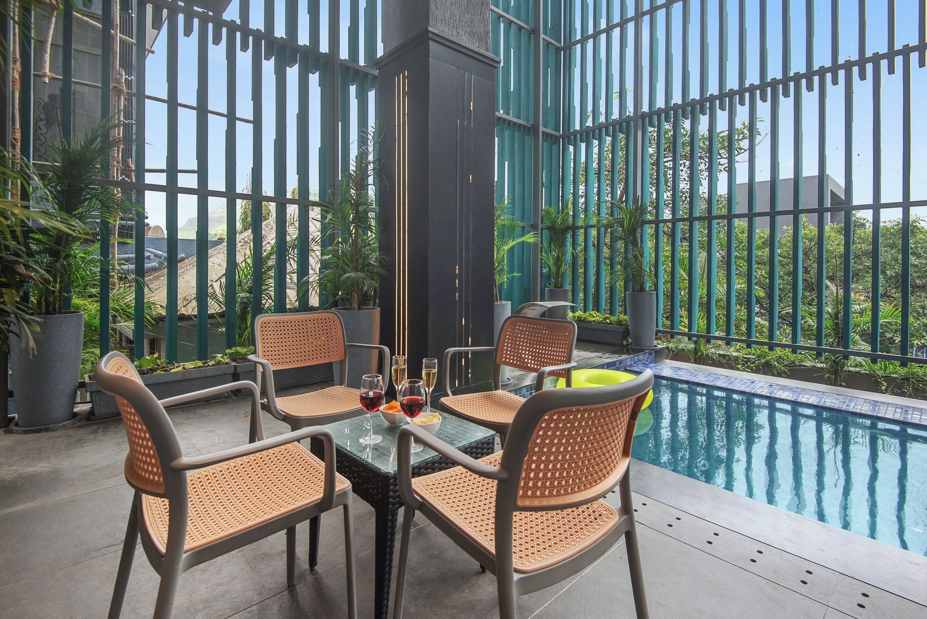 Un área de piscina interior con una mesa y sillas, rodeada de paredes de cristal y plantas en macetas.