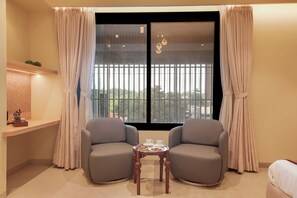 A room with two grey armchairs, a small table with cups and cookies, and a window with curtains.