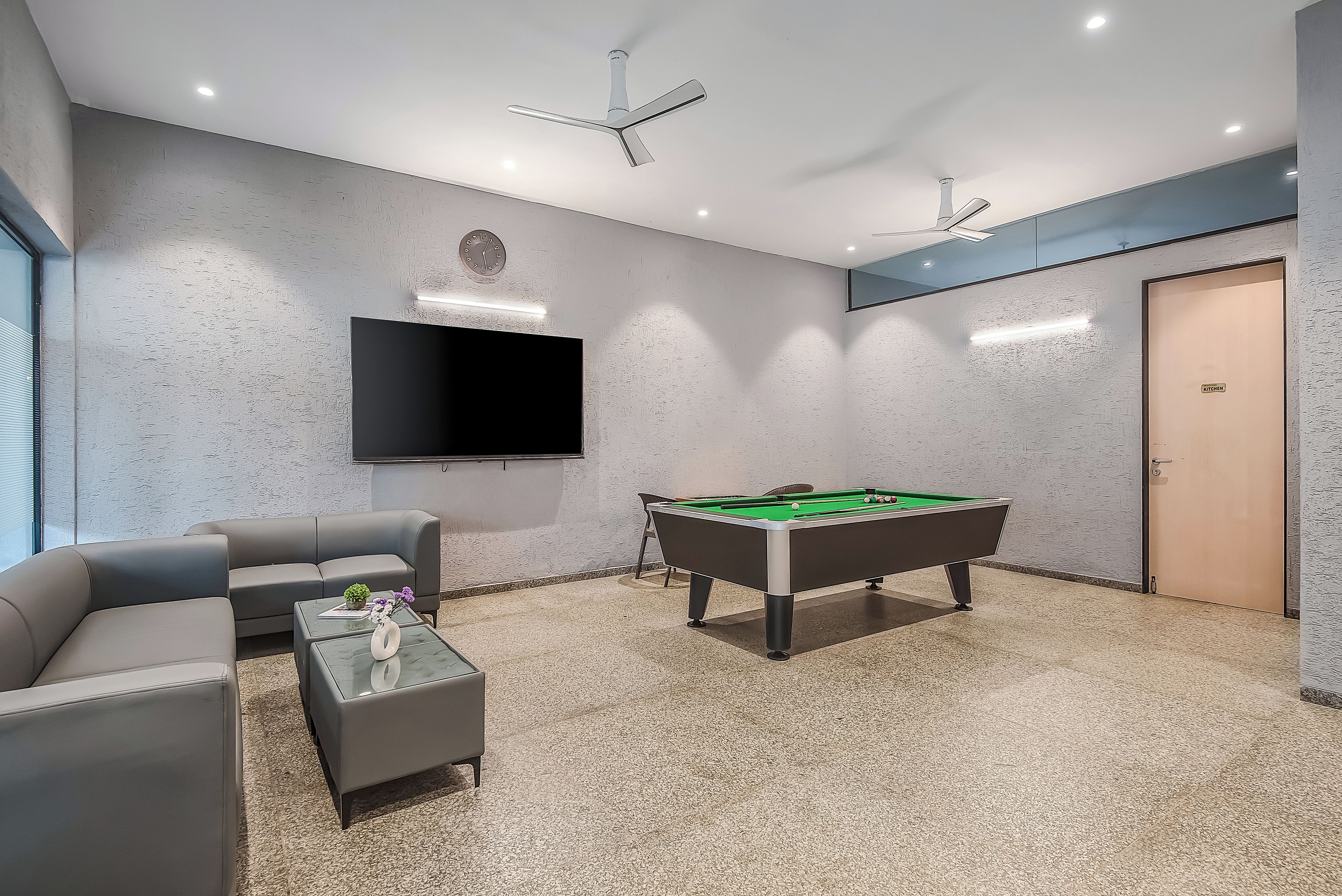 A modern room with a pool table, sofa, and a flat-screen TV mounted on the wall.