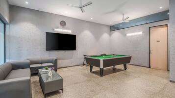 A modern room with a pool table, sofa, and a flat-screen TV mounted on the wall.