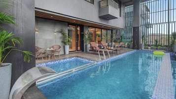 A swimming pool with lounge chairs and tables, surrounded by a building with large windows and a balcony.