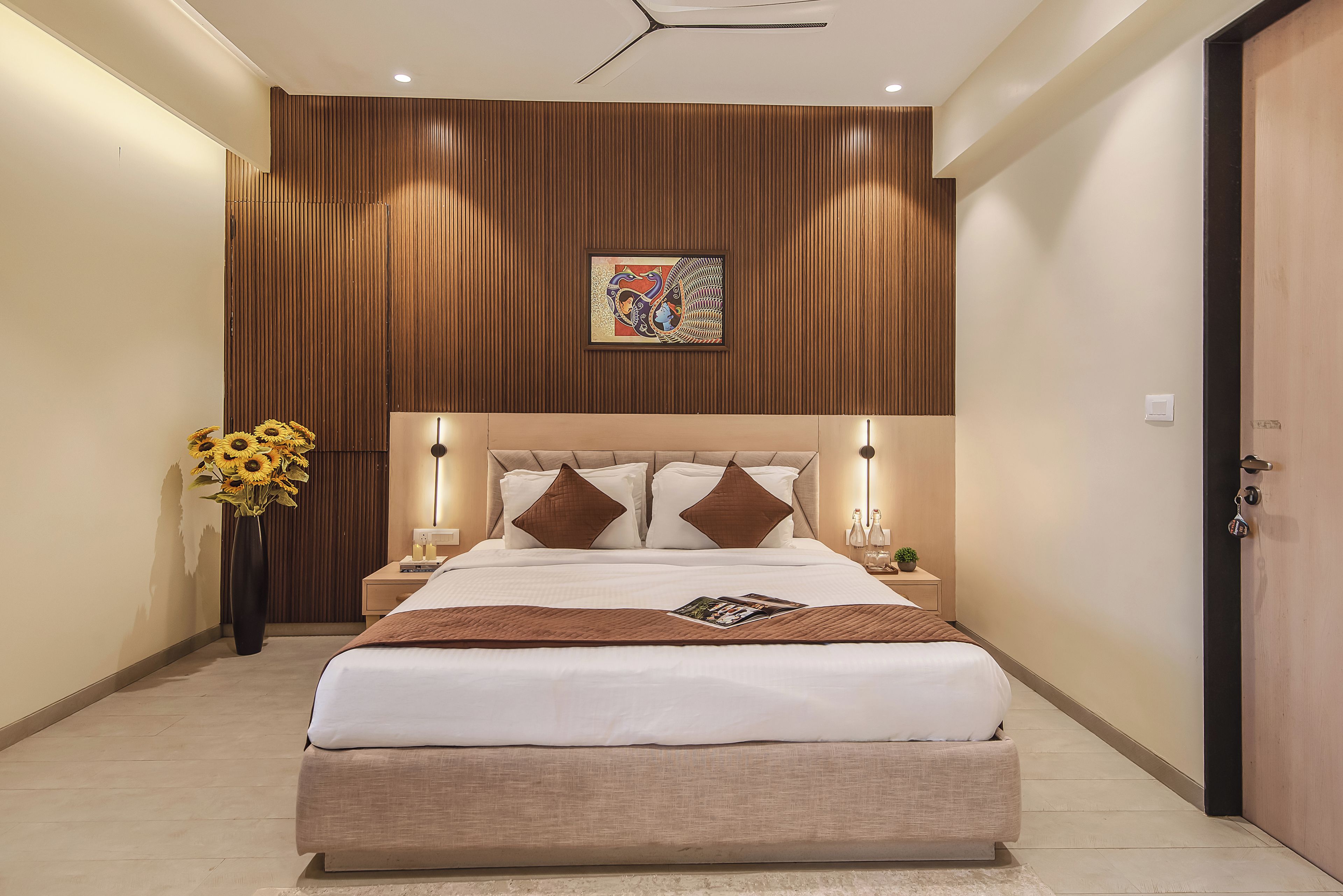 A modern hotel room with a large bed, wooden panel wall, and a decorative painting.