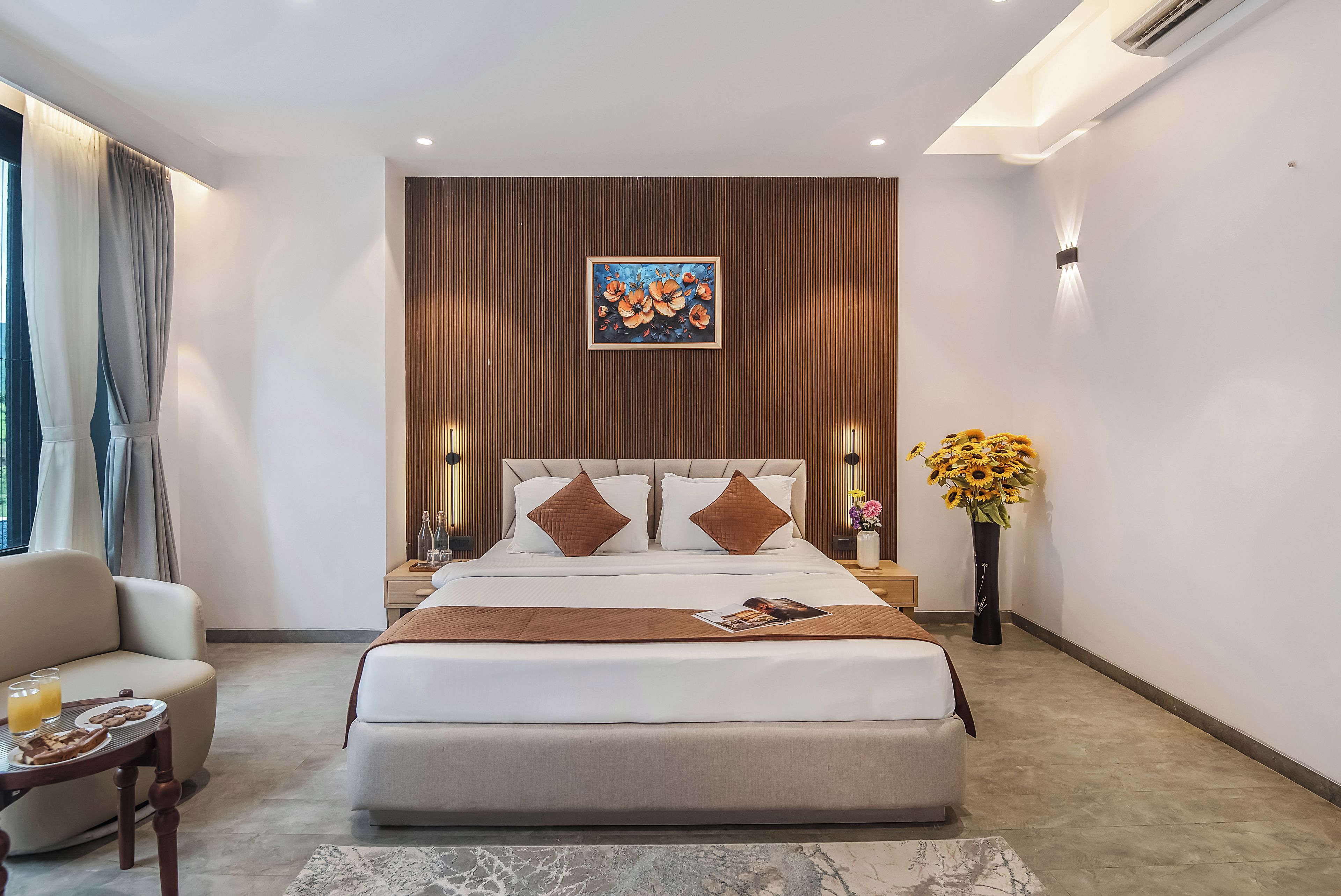 Ein modernes Schlafzimmer mit einem großen Bett, einem Nachttisch, einem Sessel, einer Vase mit Blumen und einem Bild an der Wand.