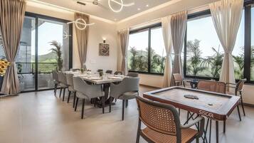 A dining area with a pool table, multiple chairs, and large windows offering a view of the outdoors.