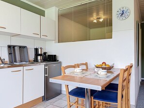 Eine kompakte Küche mit Essbereich, einer Kaffeemaschine, einem Kühlschrank und einer Wanduhr.