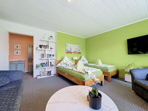 A room with two beds, a sofa, a coffee table, a bookshelf, and a TV. - Cosy apartment for 3 guests with WIFI, TV and terrace (Raben Steinfeld)