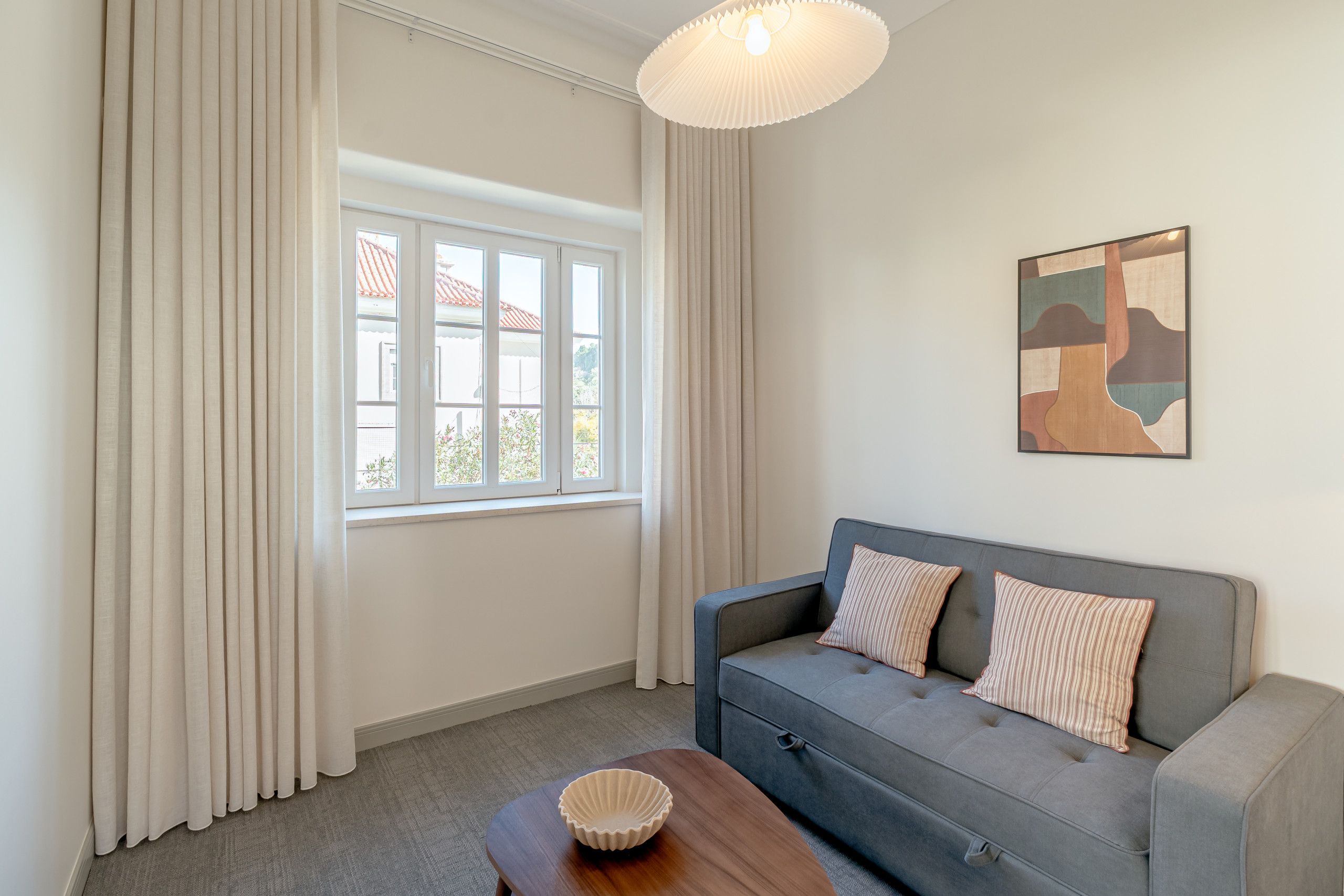 A room with a grey sofa, a wooden side table, and a wall-mounted artwork.