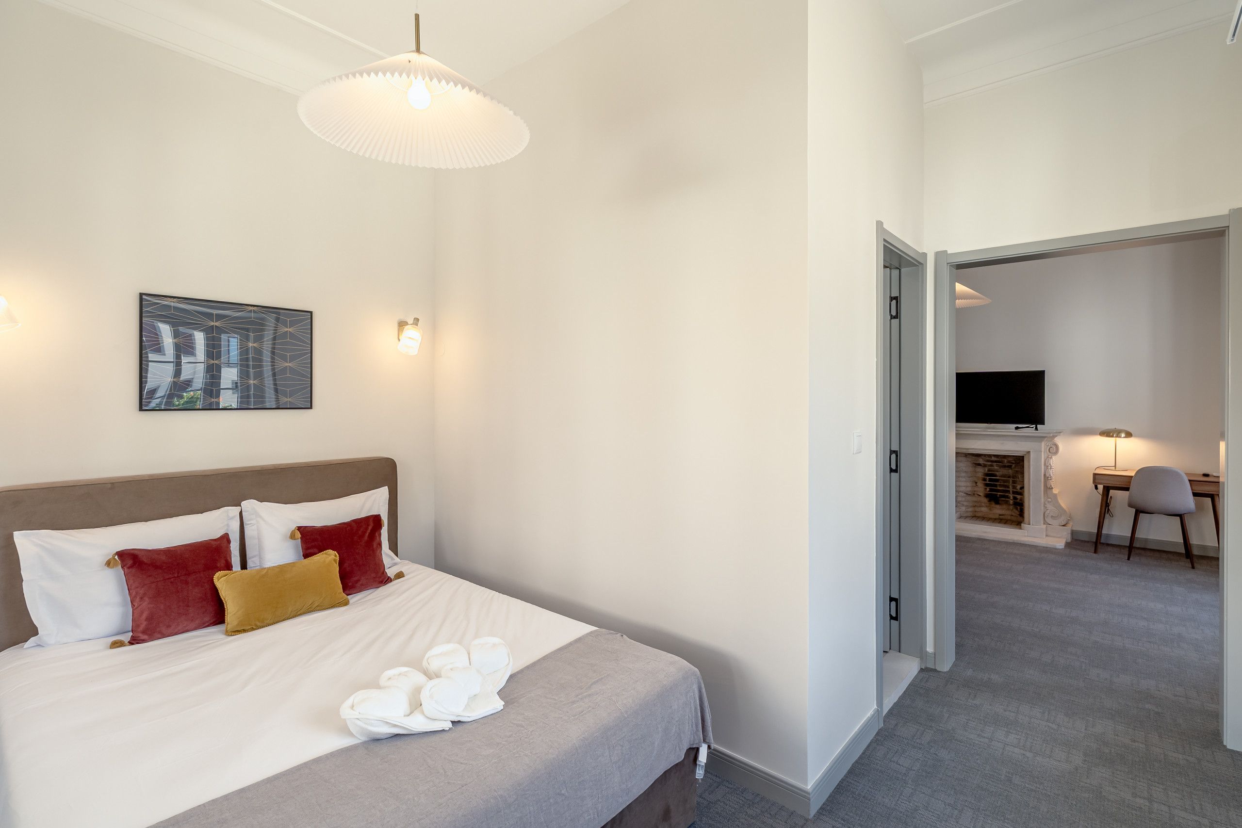 A hotel room with a bed, a painting, a desk with a chair, and a television.