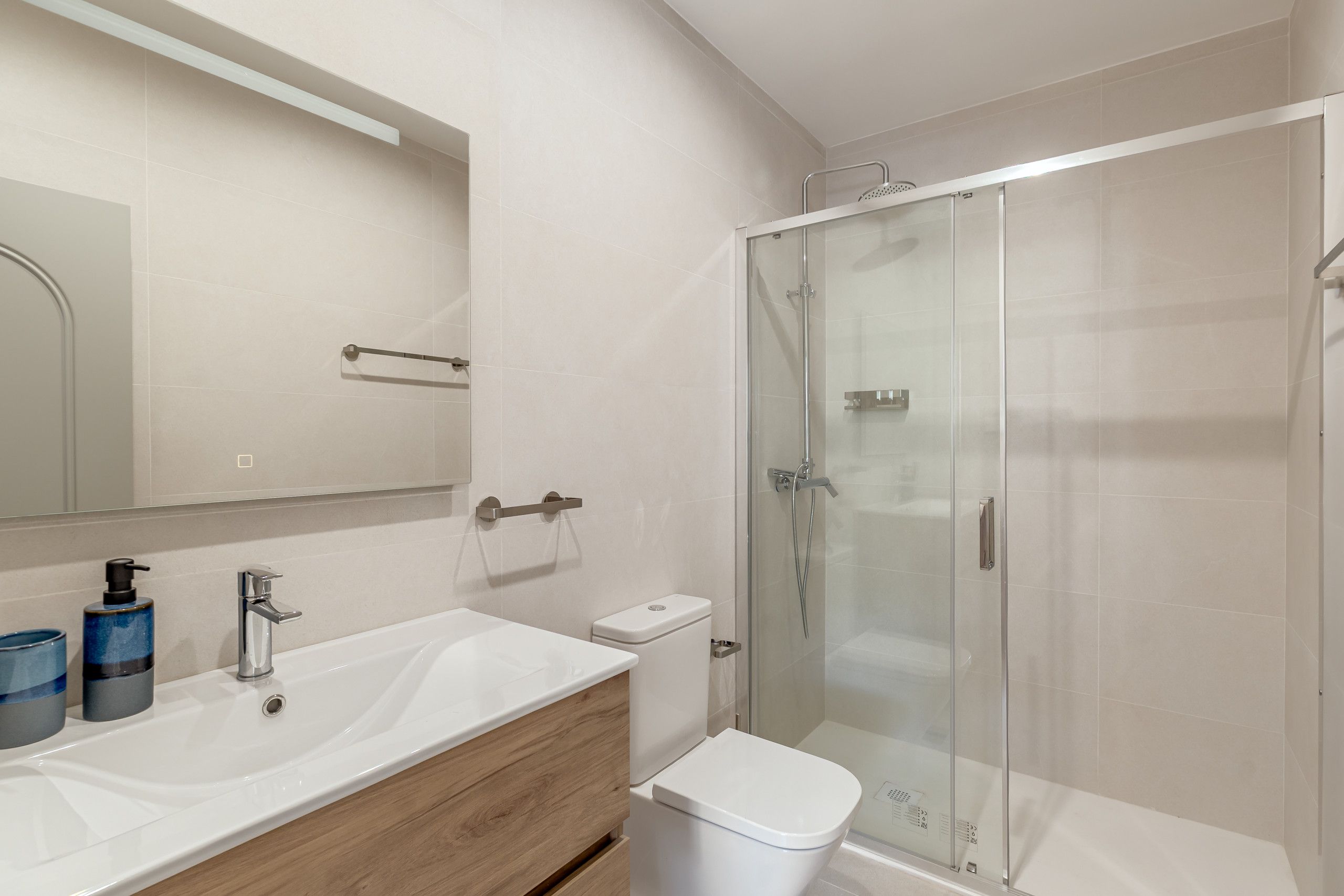 A modern bathroom with a glass-enclosed shower, a white sink, and a wooden vanity.