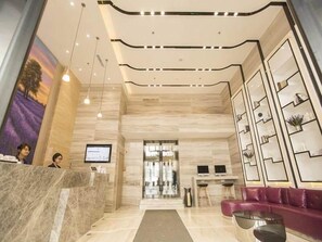 A hotel reception area with a marble reception desk, a seating area with a sofa, and a wall-mounted shelf with decorative items. - Lavande Hotels (Harbin)