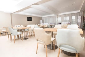 A modern dining area with round tables and chairs, a flat-screen TV mounted on the wall, and a large window with curtains. - Lavande Hotels (Harbin)
