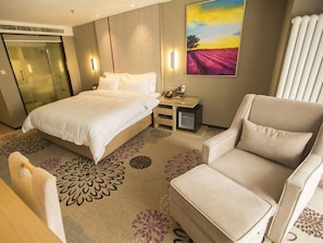 A hotel room with a bed, a chair, a desk, a small table, and a painting on the wall. - Lavande Hotels (Harbin)