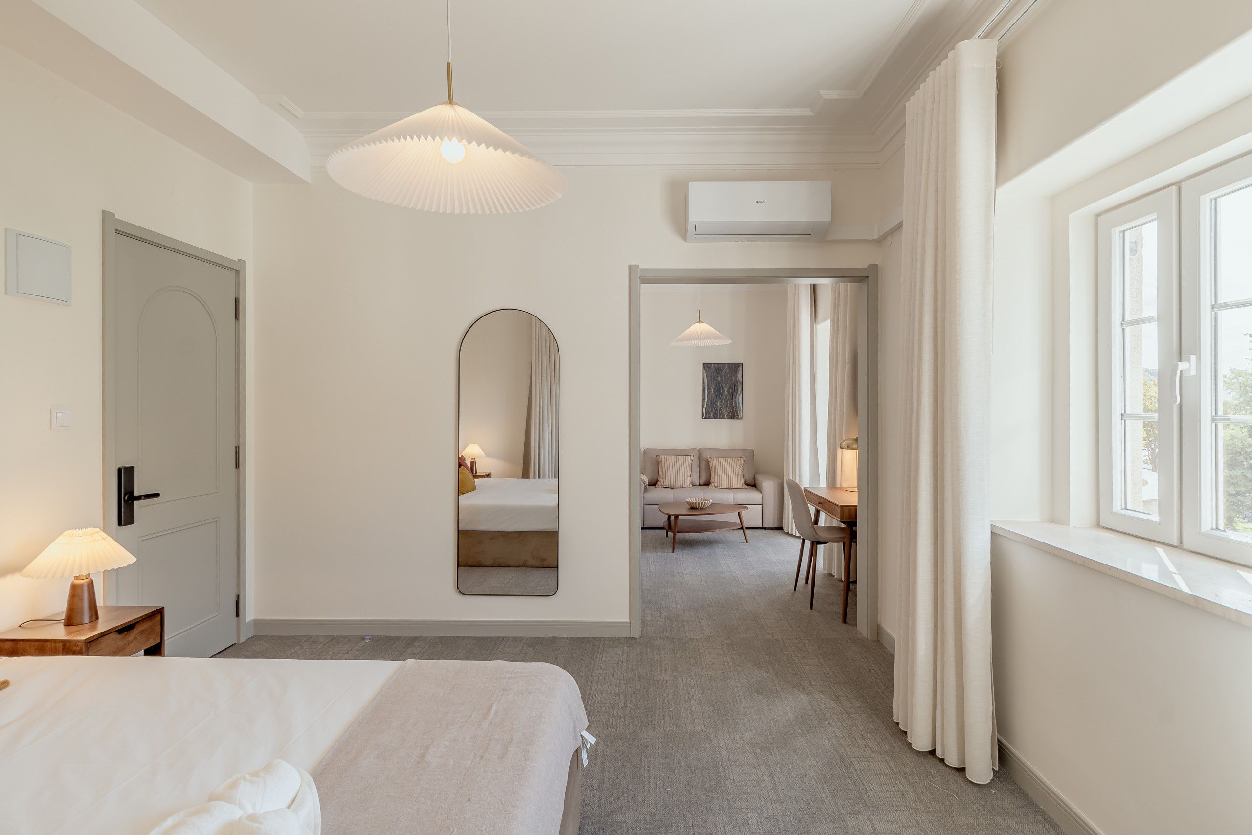 A hotel room with a bed, a desk, a chair, a mirror, and a window.