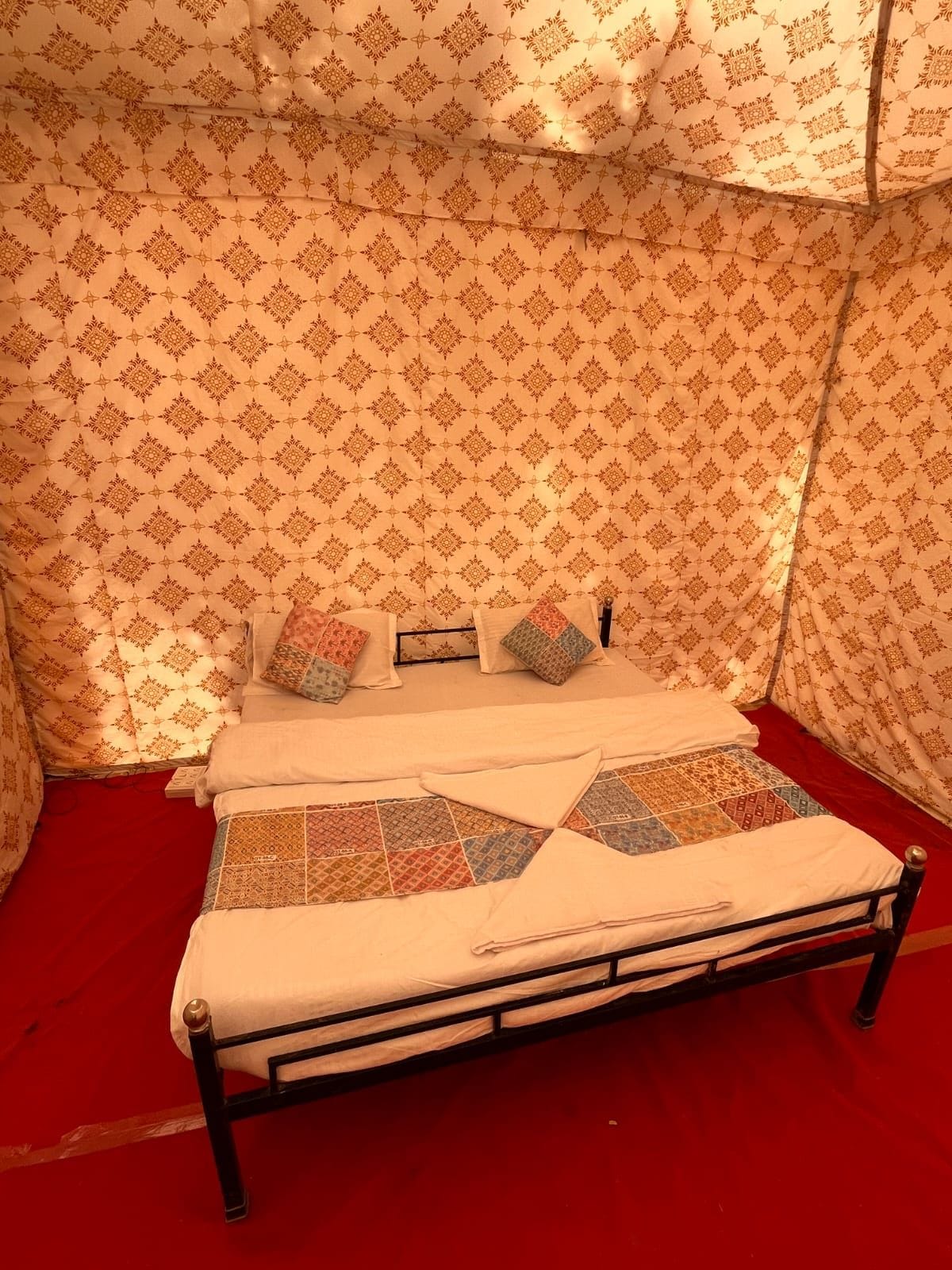 Una cama con una colcha estampada, almohadas y una alfombra roja.